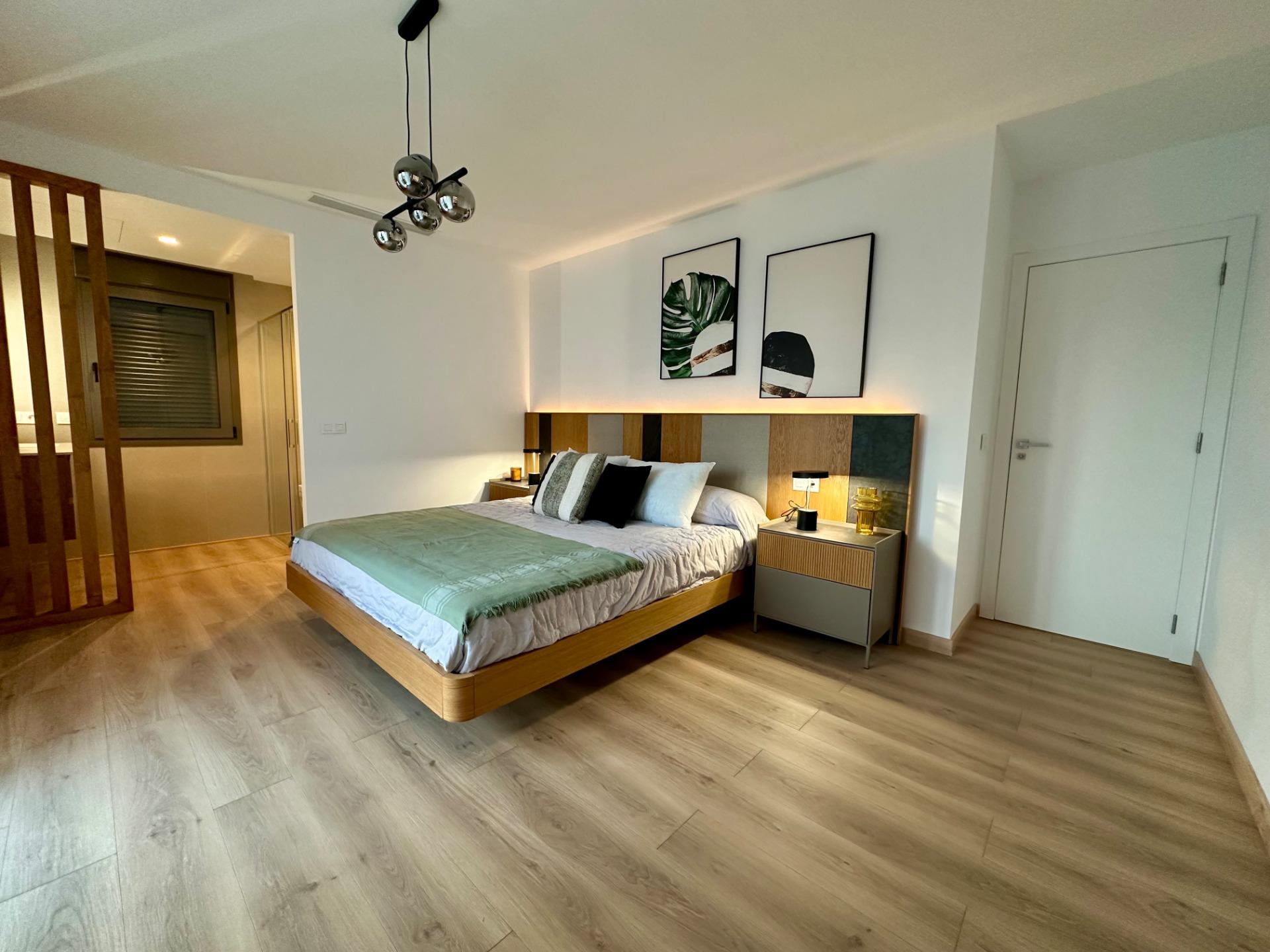 Modern bedroom with a low wooden bed, green bed runner, and two nightstands beneath framed botanical art.