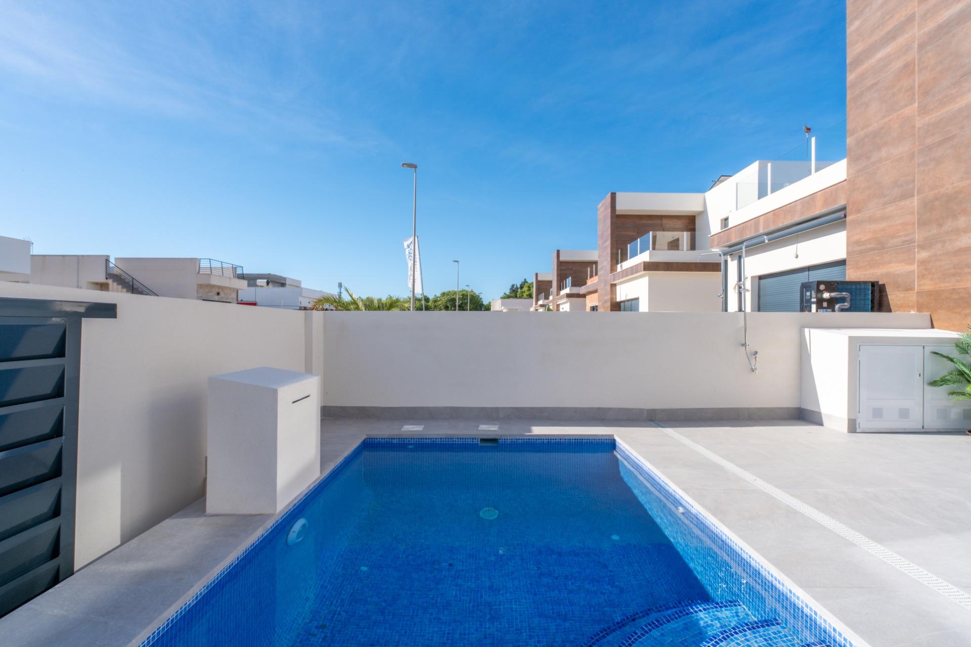 Rectangular blue pool surrounded by white walls and modern apartments under a clear blue sky.