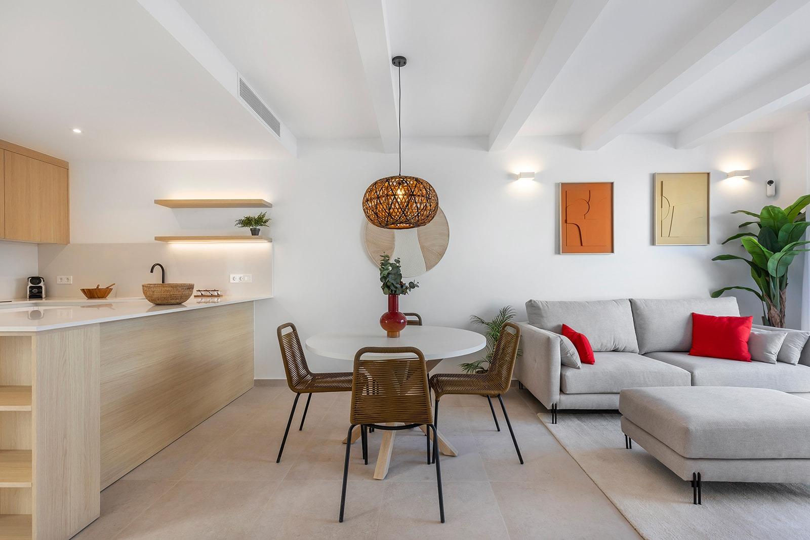 Open-plan living space with a round dining table, wicker chairs, and a woven pendant light over the table.