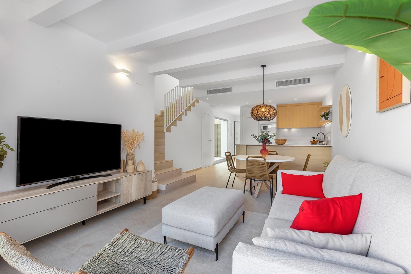 Living room with white walls, a gray sofa with red cushions, and a flat-screen TV on a light wood console.