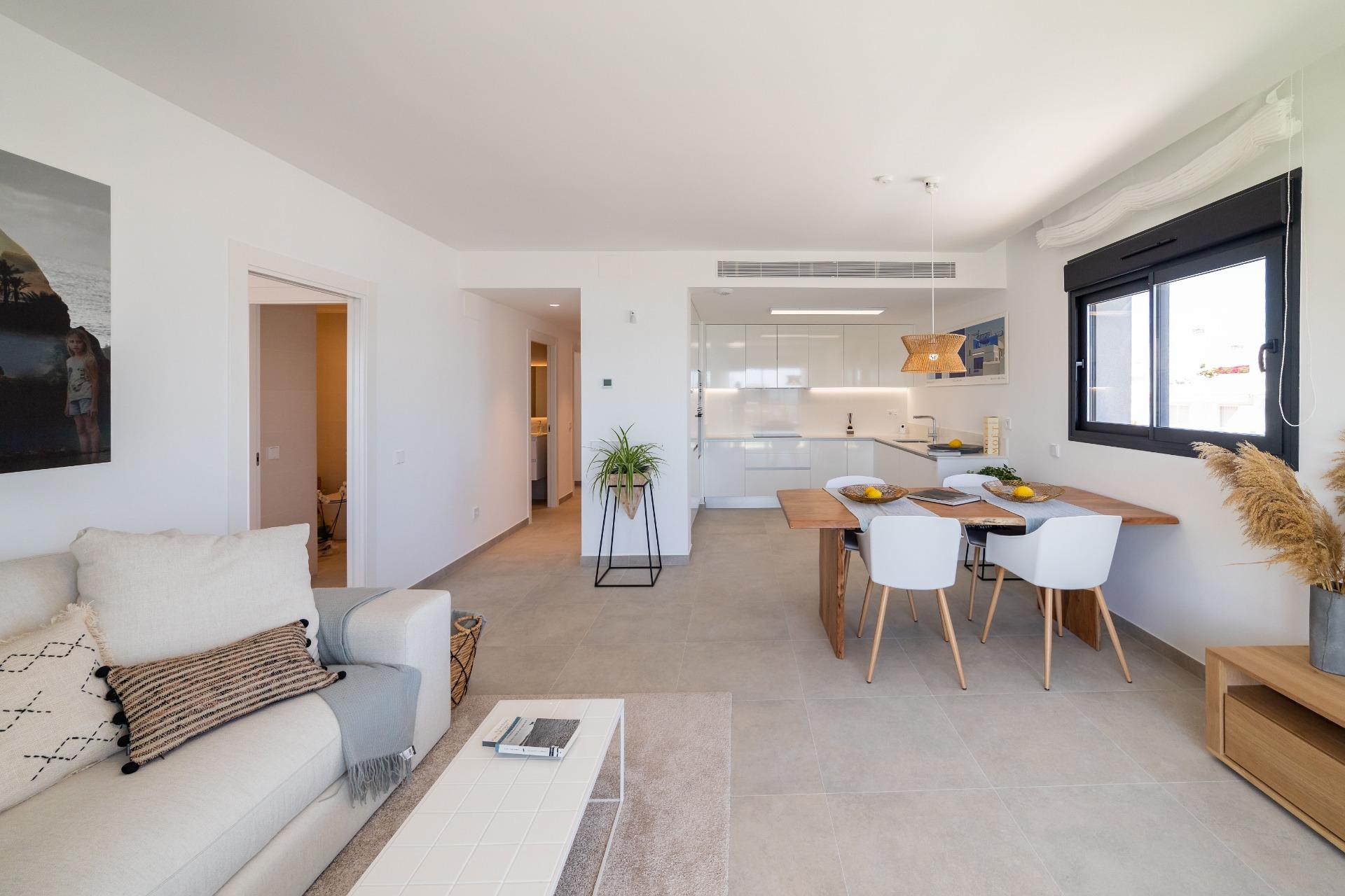 Open-plan living space with a beige sofa, white walls, and a wooden dining table near a large window on the right.