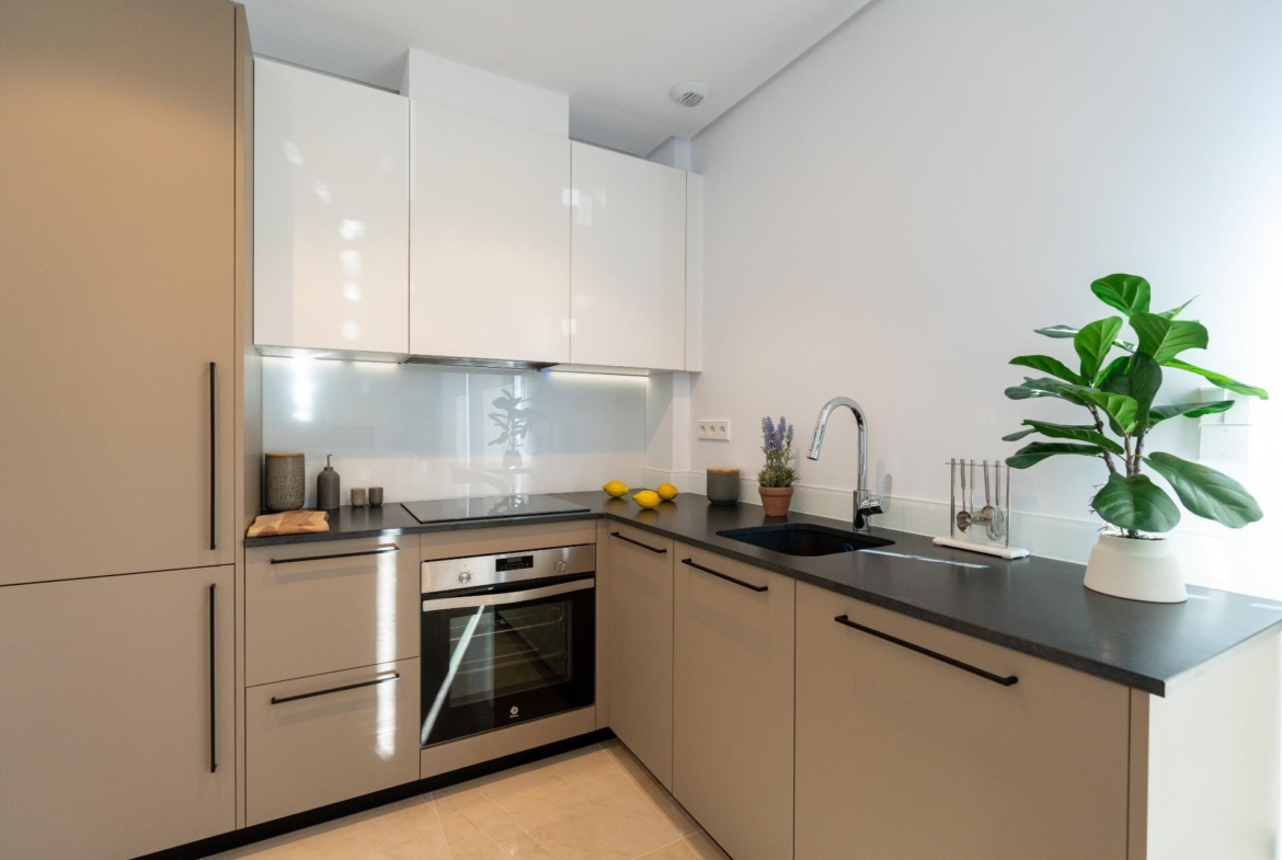Modern L-shaped kitchen with grey lower cabinets, white wall cabinets, and a black countertop; sink and lemon accents on the counter.