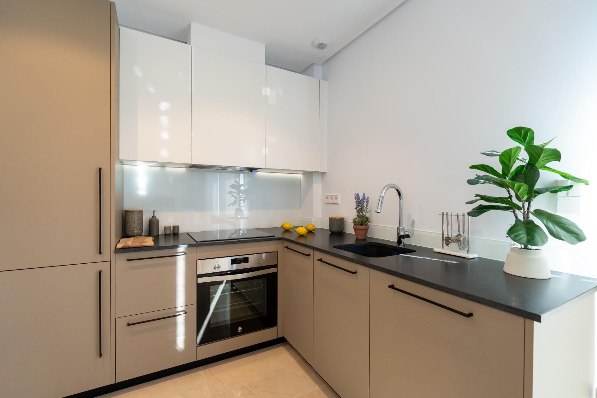 Modern L-shaped kitchen with grey lower cabinets, white wall cabinets, and a black countertop; sink and lemon accents on the counter.