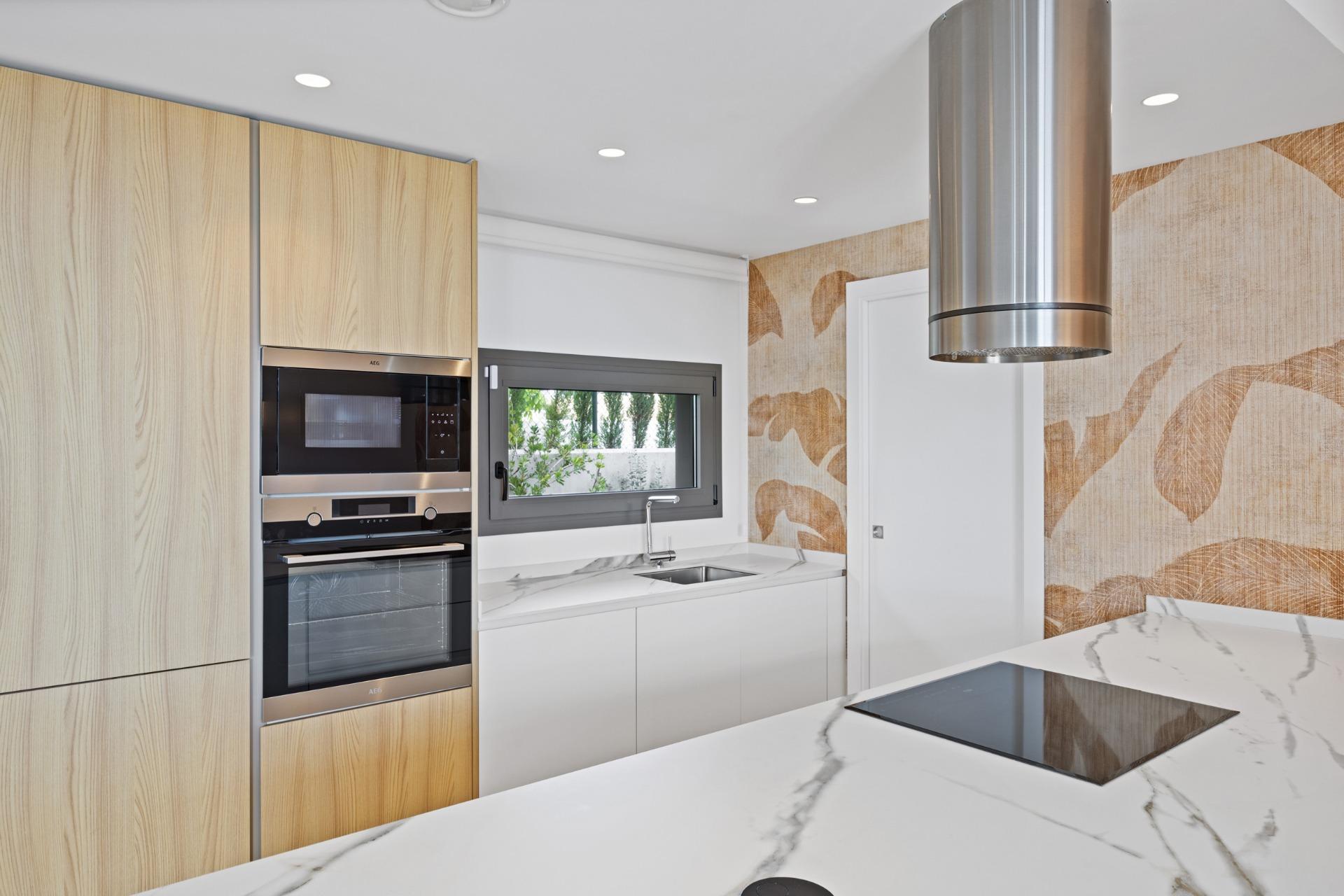 Modern kitchen with tall light-wood cabinets, built-in stainless oven and microwave, white marble countertop, and a cylindrical stainless range hood.