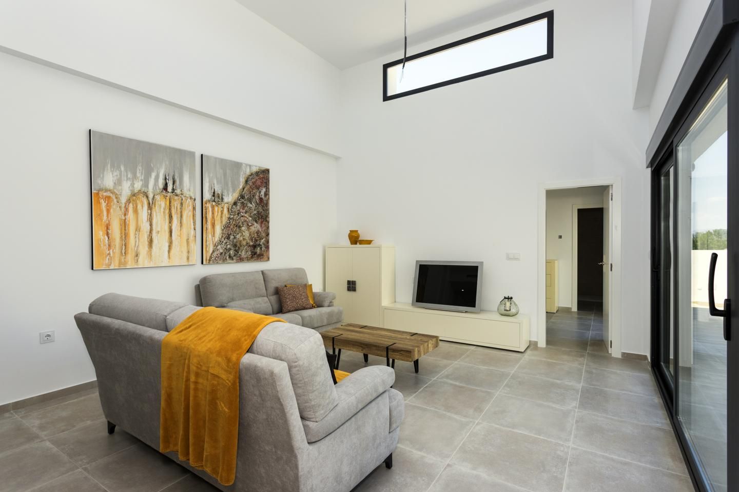 Modern living room with two gray sofas, an orange throw, and a wooden coffee table under abstract wall art. A TV sits on a low white cabinet against the wall.