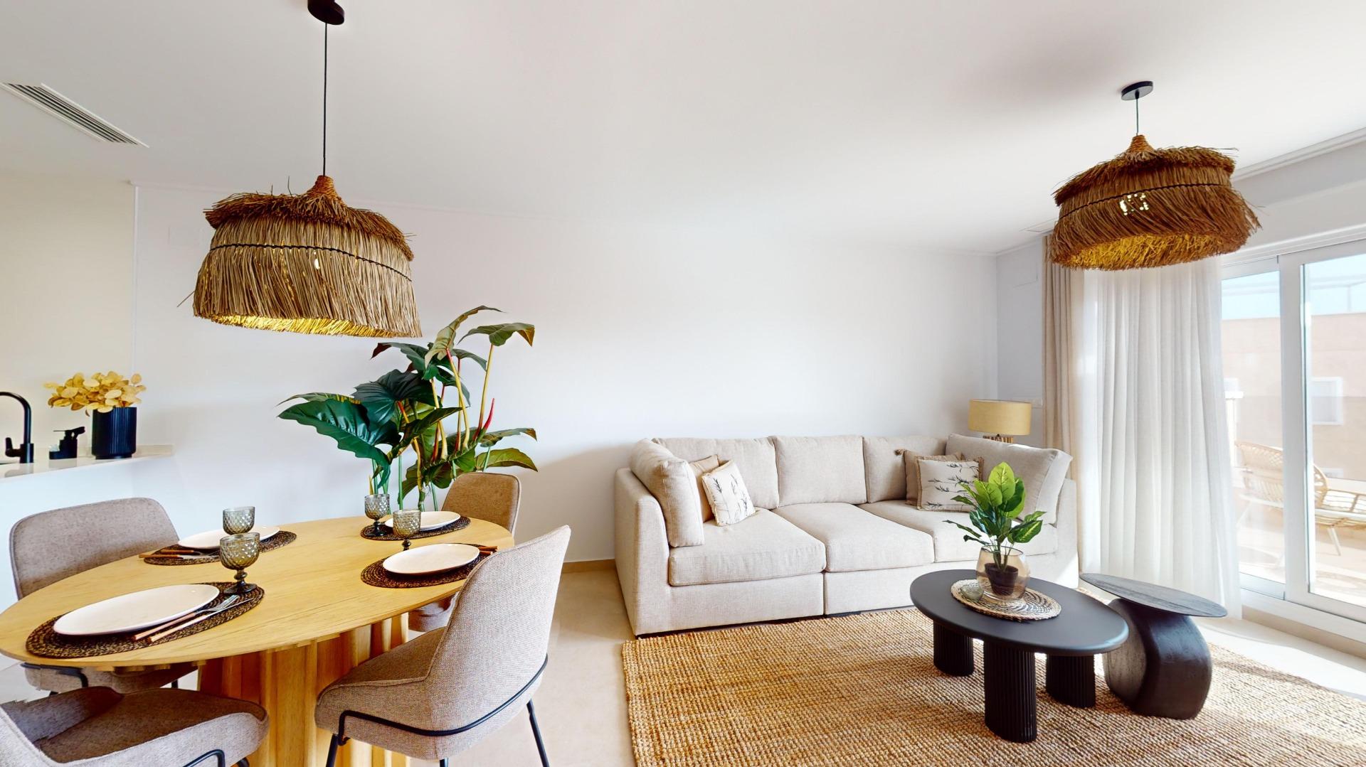 Bright open living and dining area with a beige sectional, round wooden dining table, and woven straw pendant lights. A large plant and curtains frame a sunny space.